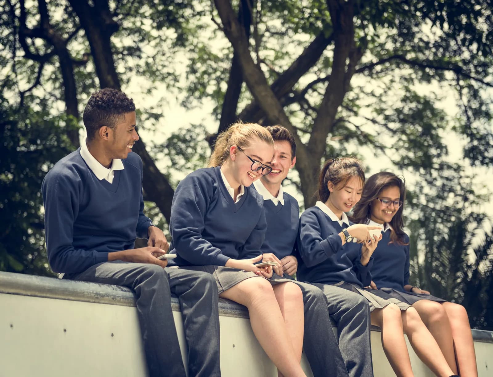 Teenagers sitting together outdoors while using their phones