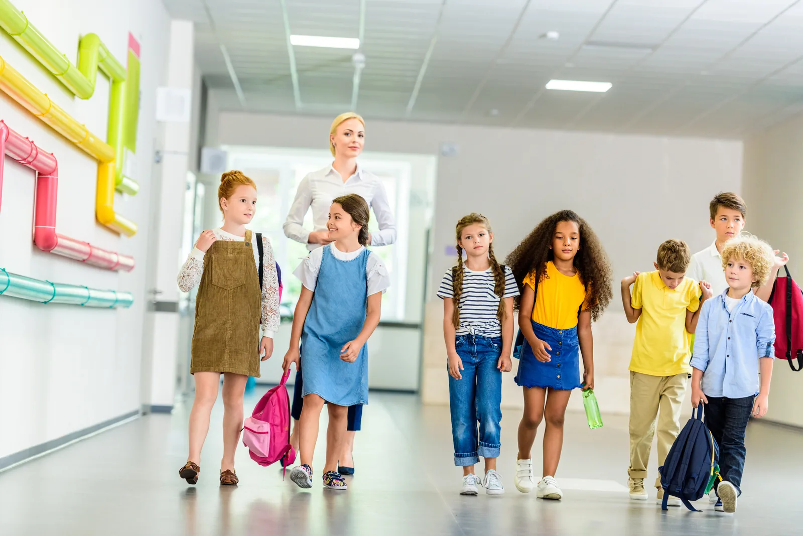 Elementary students walking with a teacher through a school hallway