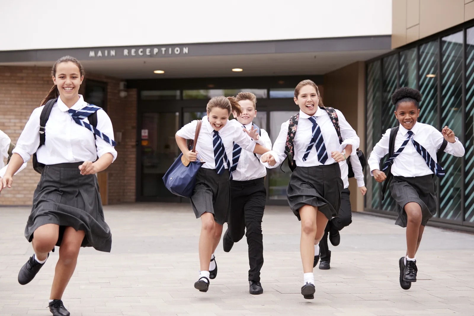 High school students running outside school with backpacks