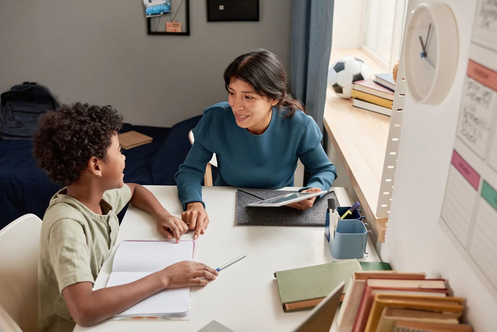 A student and tutor reviewing schoolwork together at a desk at home