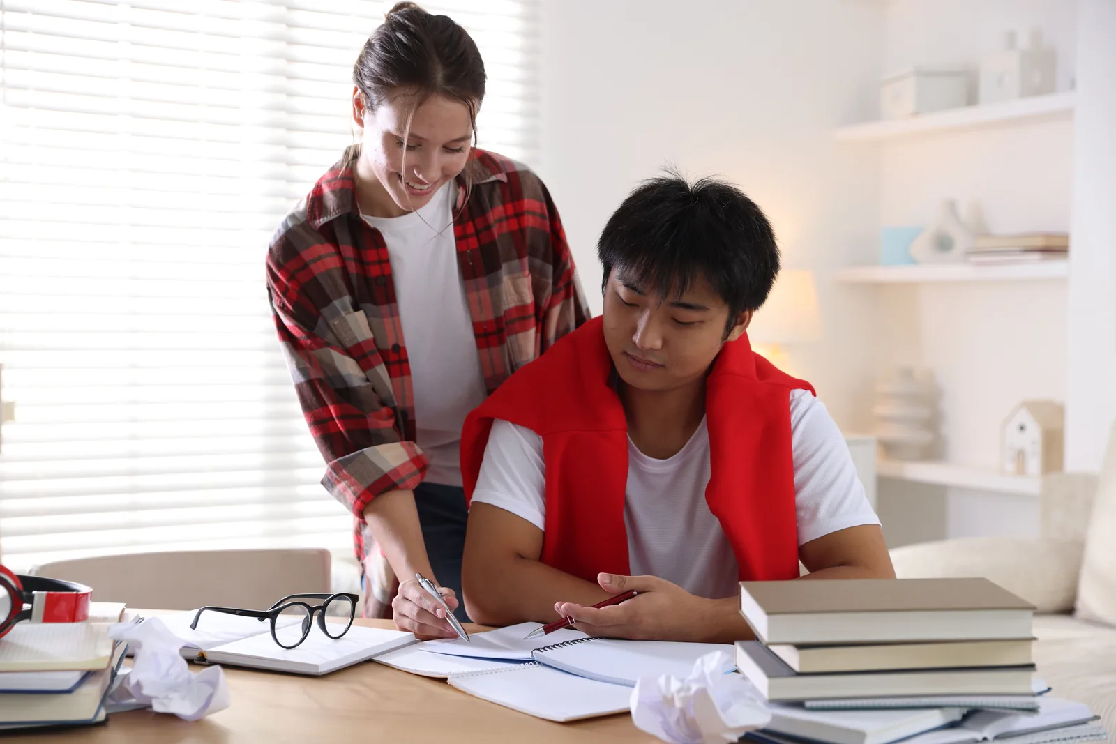 High school student writing at a desk while an adult provides support