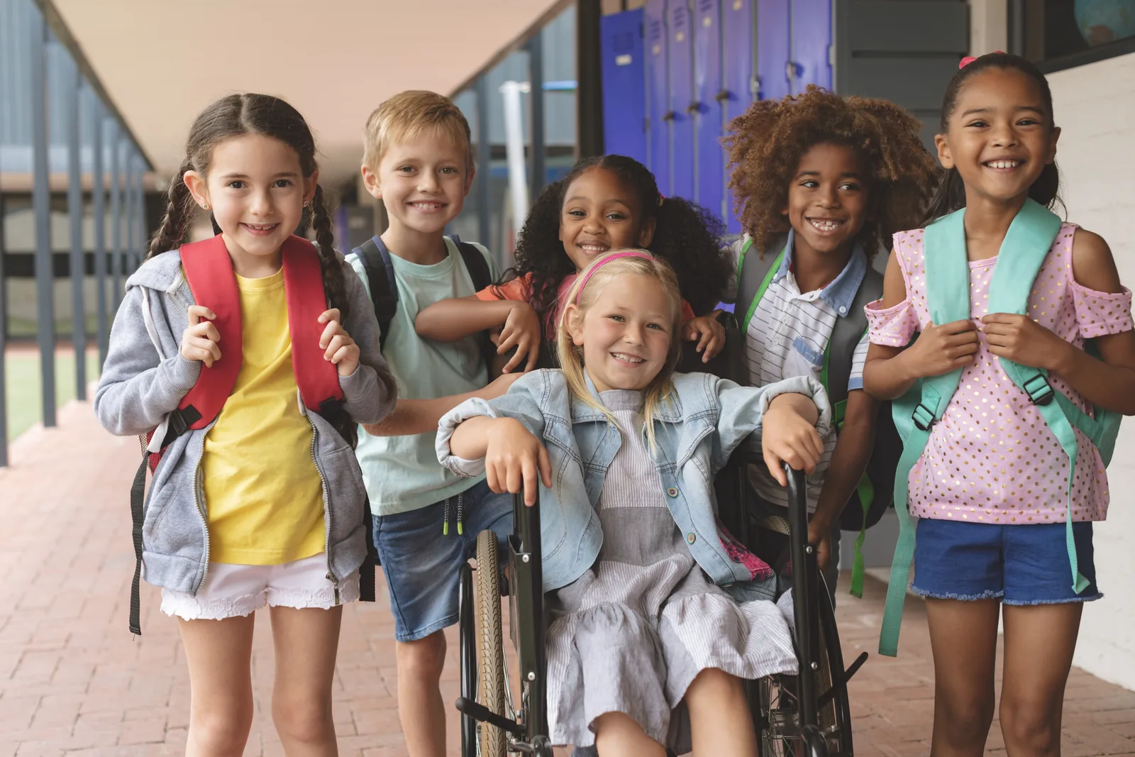 Diverse elementary students including a wheelchair user standing outside school