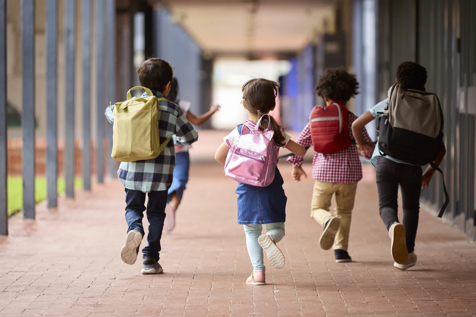 Students running down a covered school walkway with backpacks