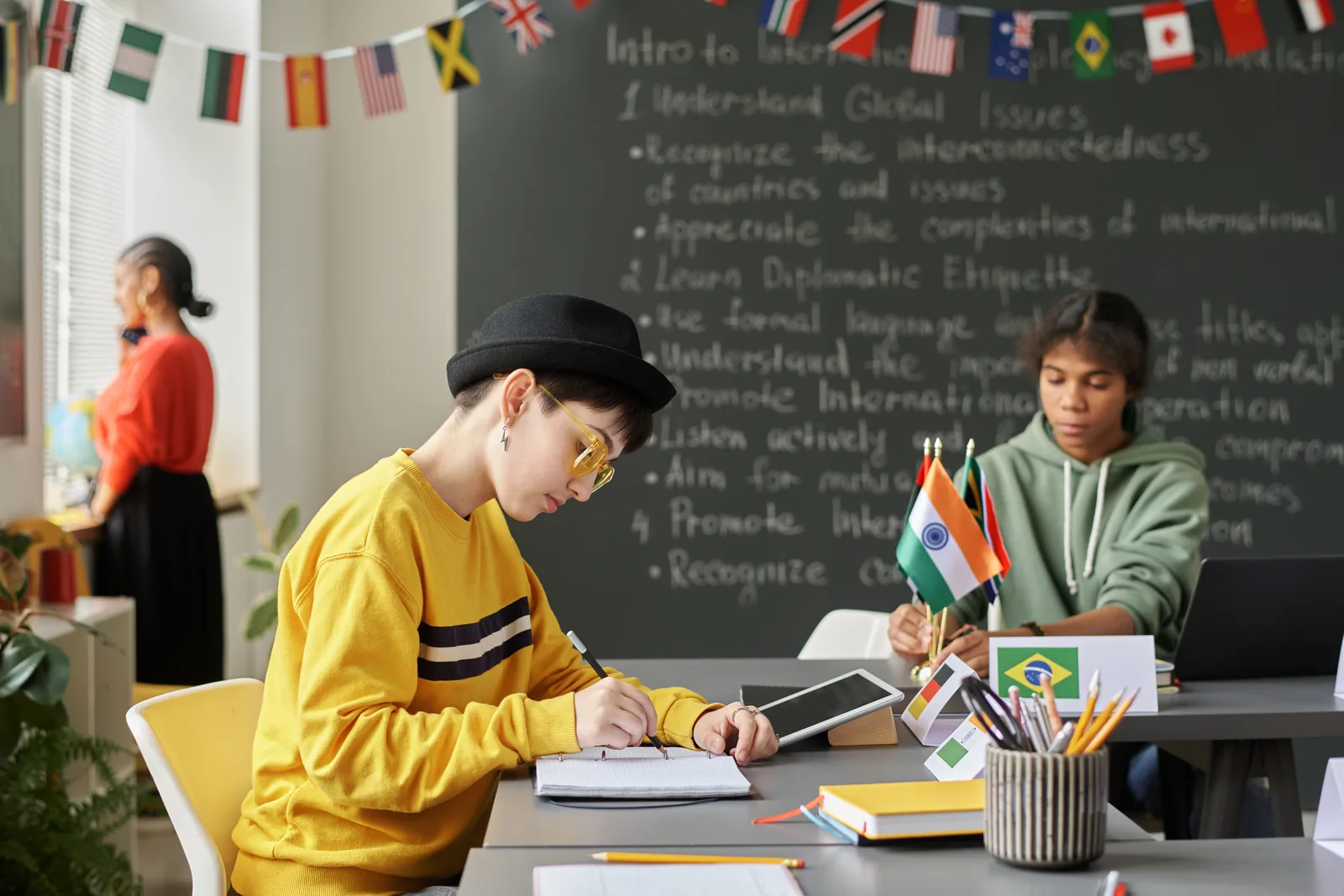 Two students writing independently at desks in a classroom with international flags