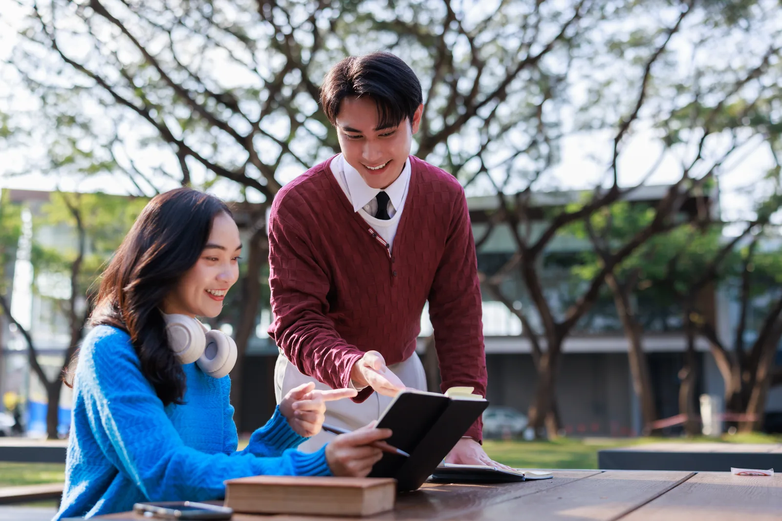 Two older students using a tablet and books together outdoors