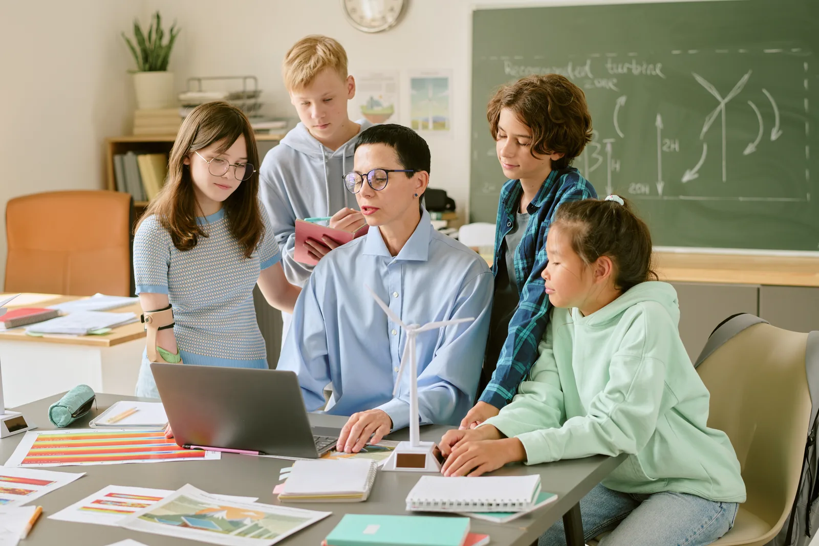 A teacher and middle-school students examining a small wind-turbine model and data