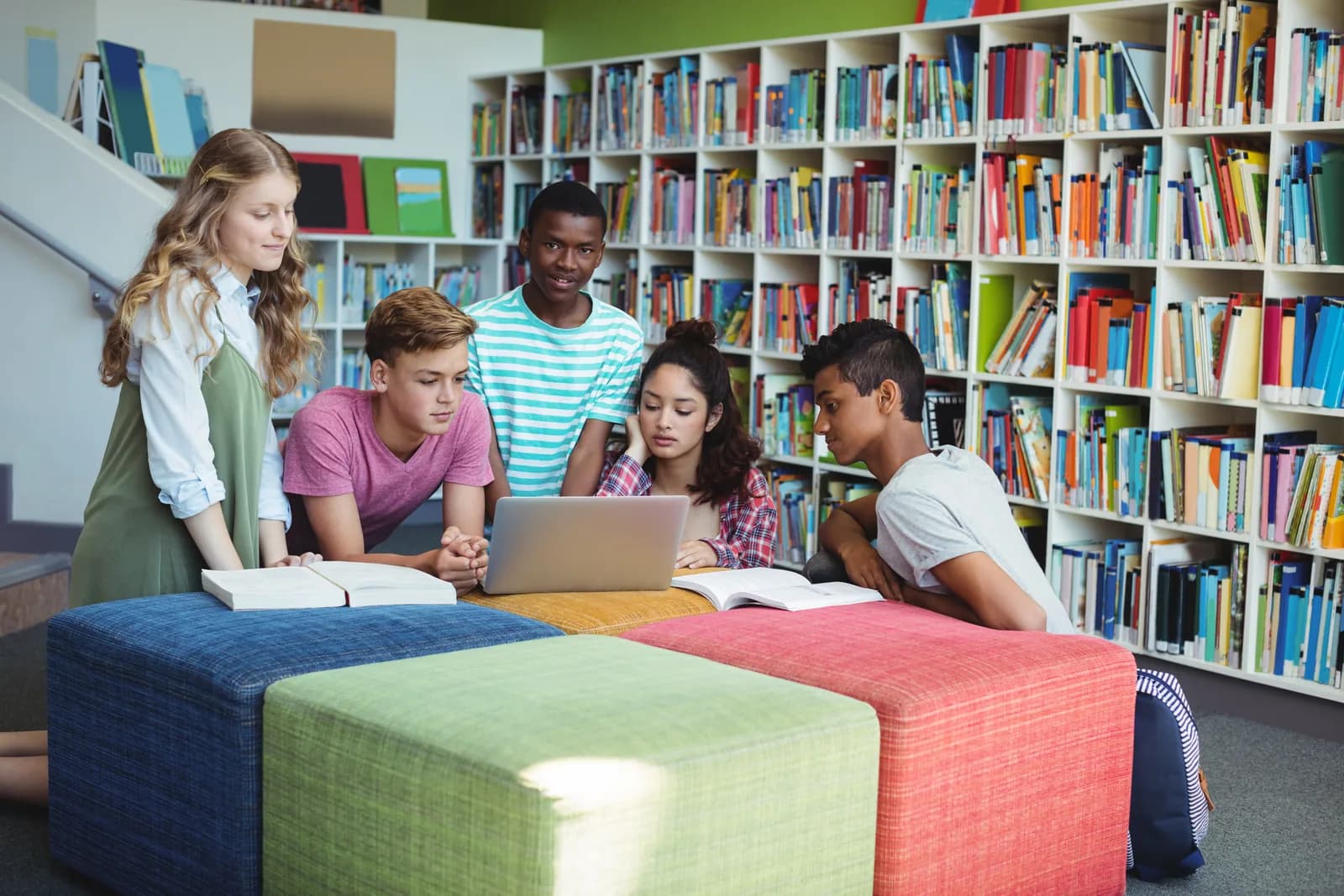 Uczniowie wspólnie pracują przy laptopie i książkach w bibliotece